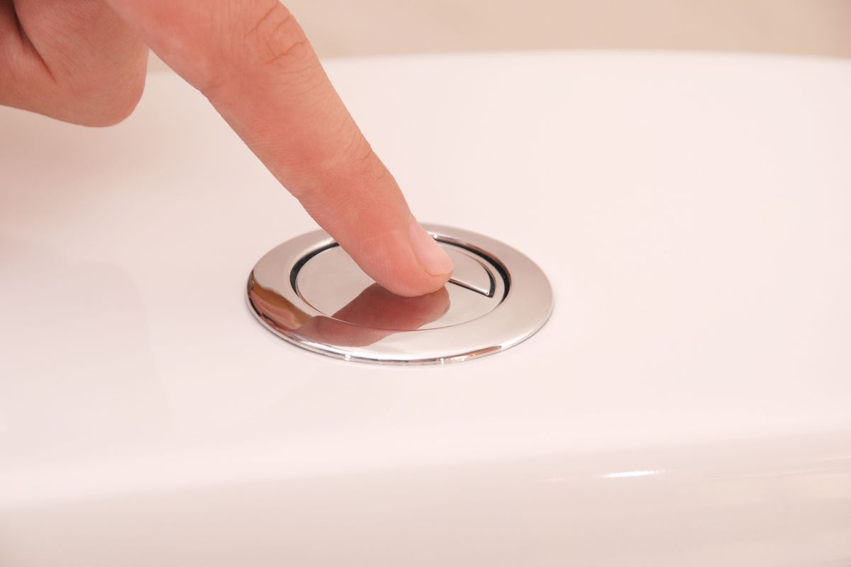 Gros plan sur une main appuyant sur le bouton poussoir d'une chasse d'eau