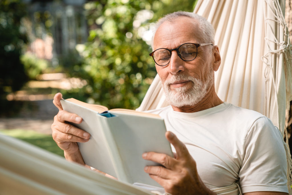 Homme âgé détendu dans un hamac, en train de lire un livre